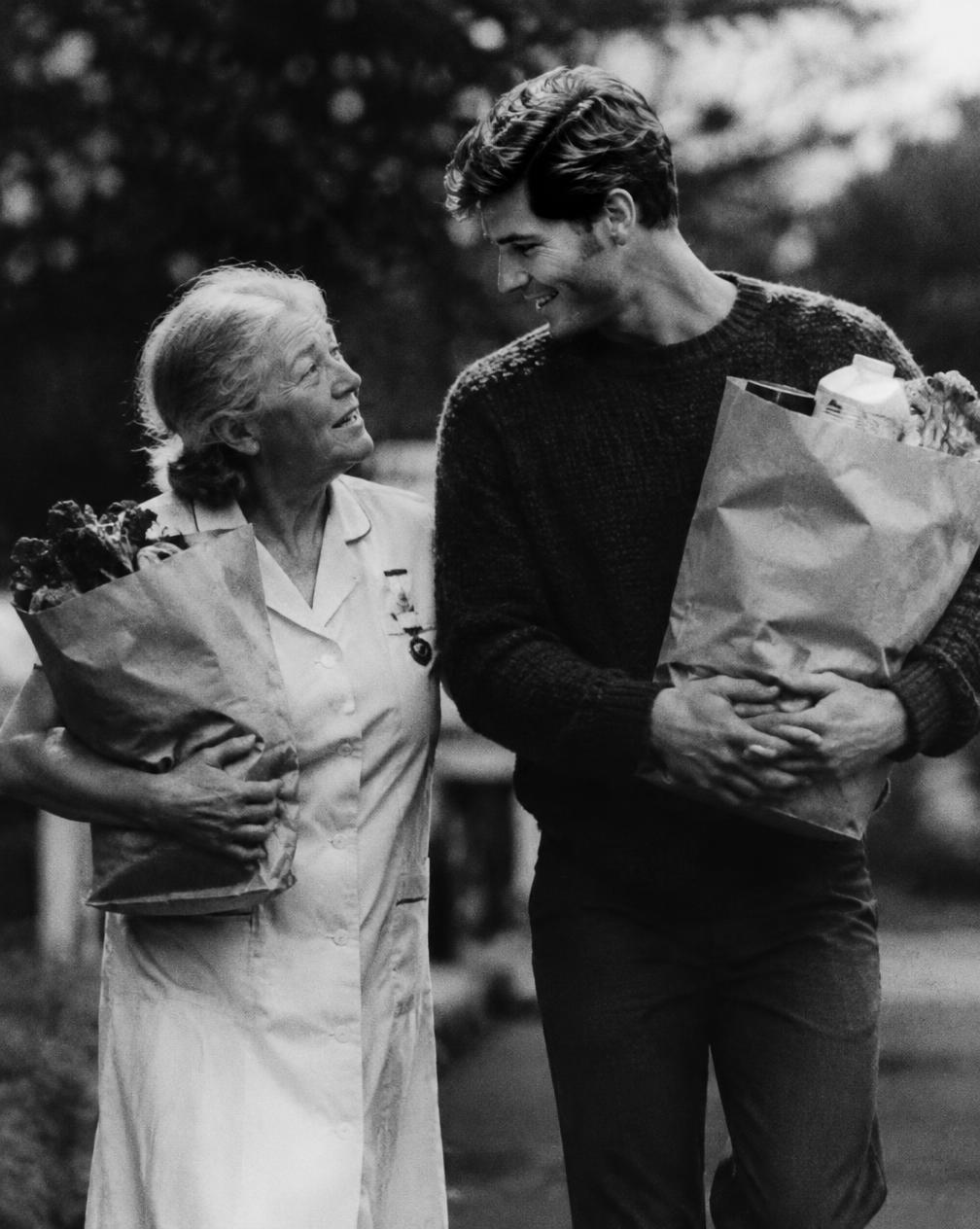 An older nurse and a young man carrying groceries together